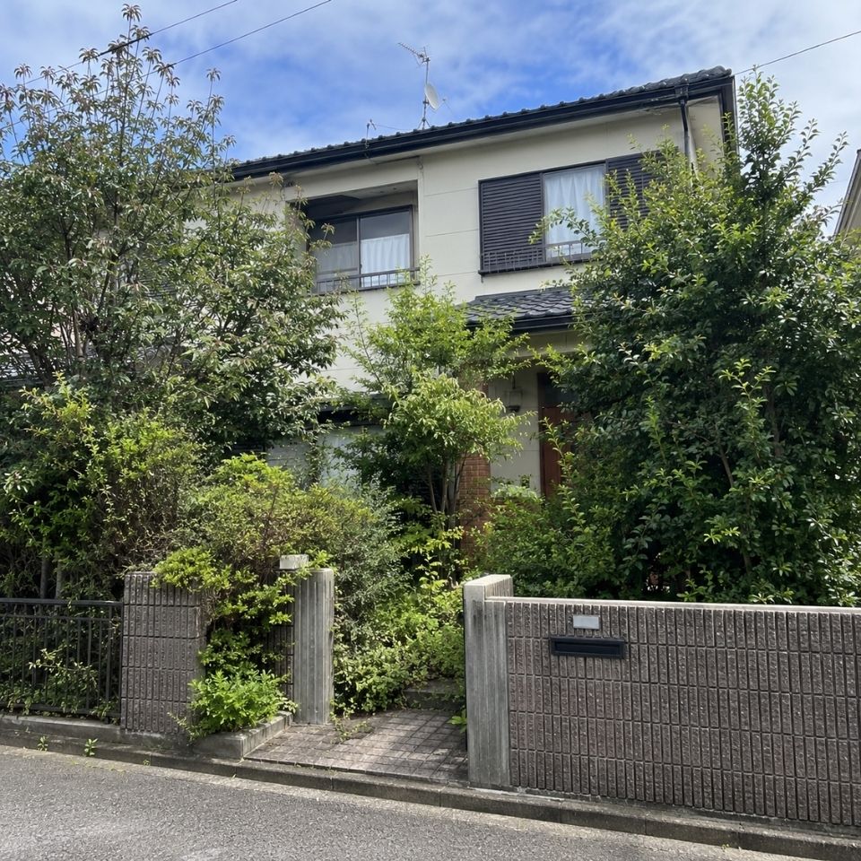 手入れ前で枝葉が伸びた庭木と住宅外観の写真